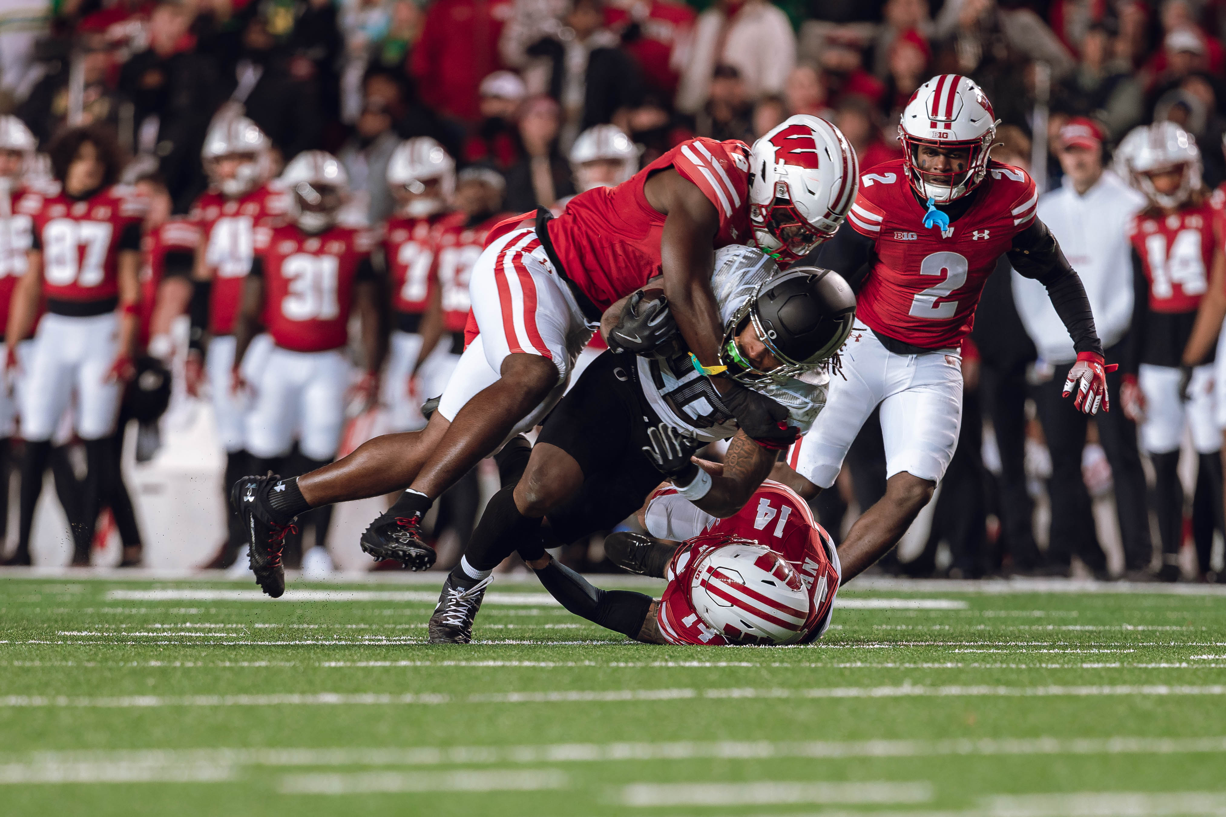 Oregon running back Jordan James #20 gets taken down by Wisconsin Badgers outside linebacker Leon Lowery Jr. #8 & Wisconsin Badgers safety Preston Zachman #14 at Camp Randall Stadium on November 16, 2024 in Madison, Wisconsin. Photography by Ross Harried for Second Crop Sports.