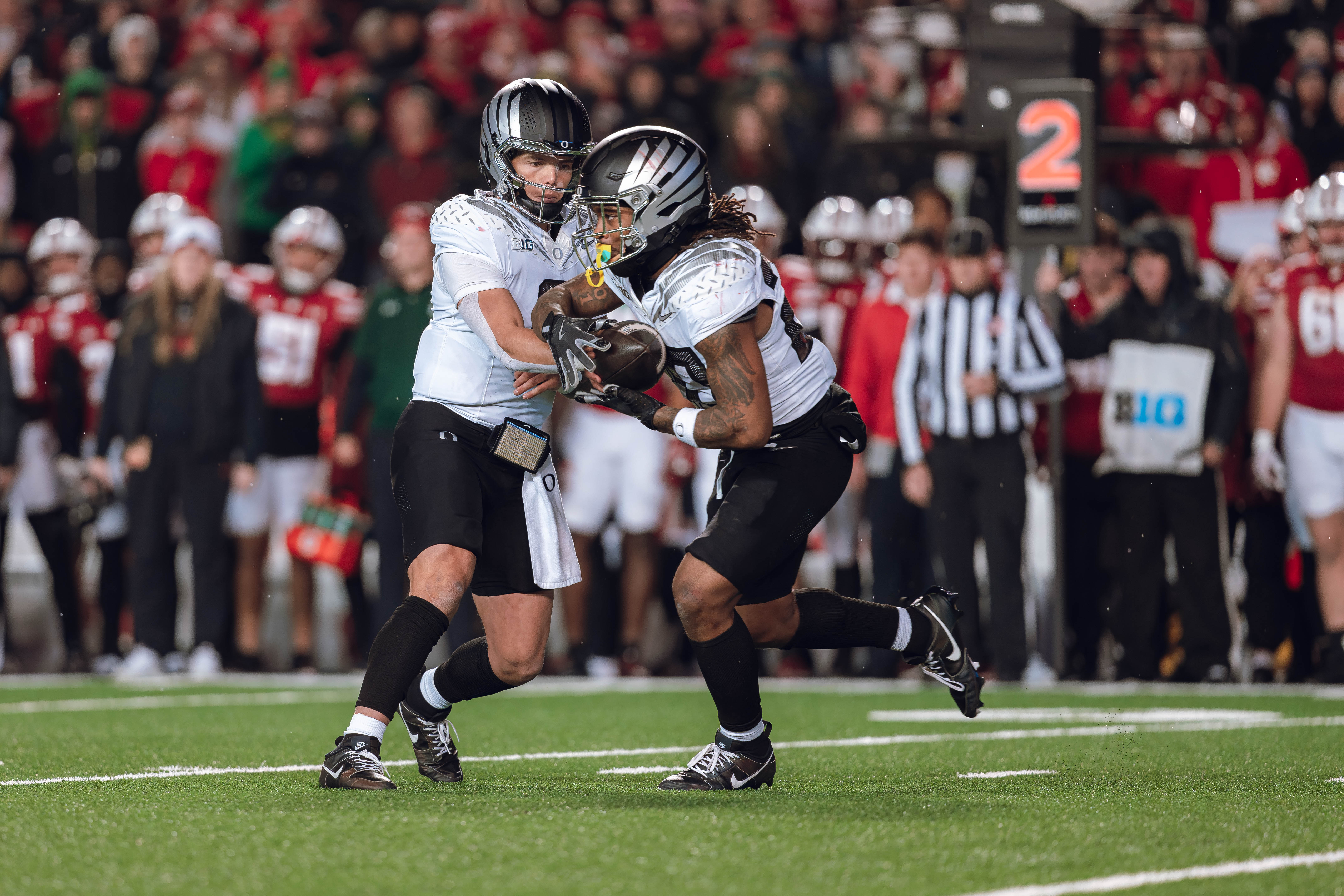 Oregon quarterback Dillon Gabriel #8 hands the ball off to Oregon running back Jordan James #20 against the Wisconsin Badgers at Camp Randall Stadium on November 16, 2024 in Madison, Wisconsin. Photography by Ross Harried for Second Crop Sports.