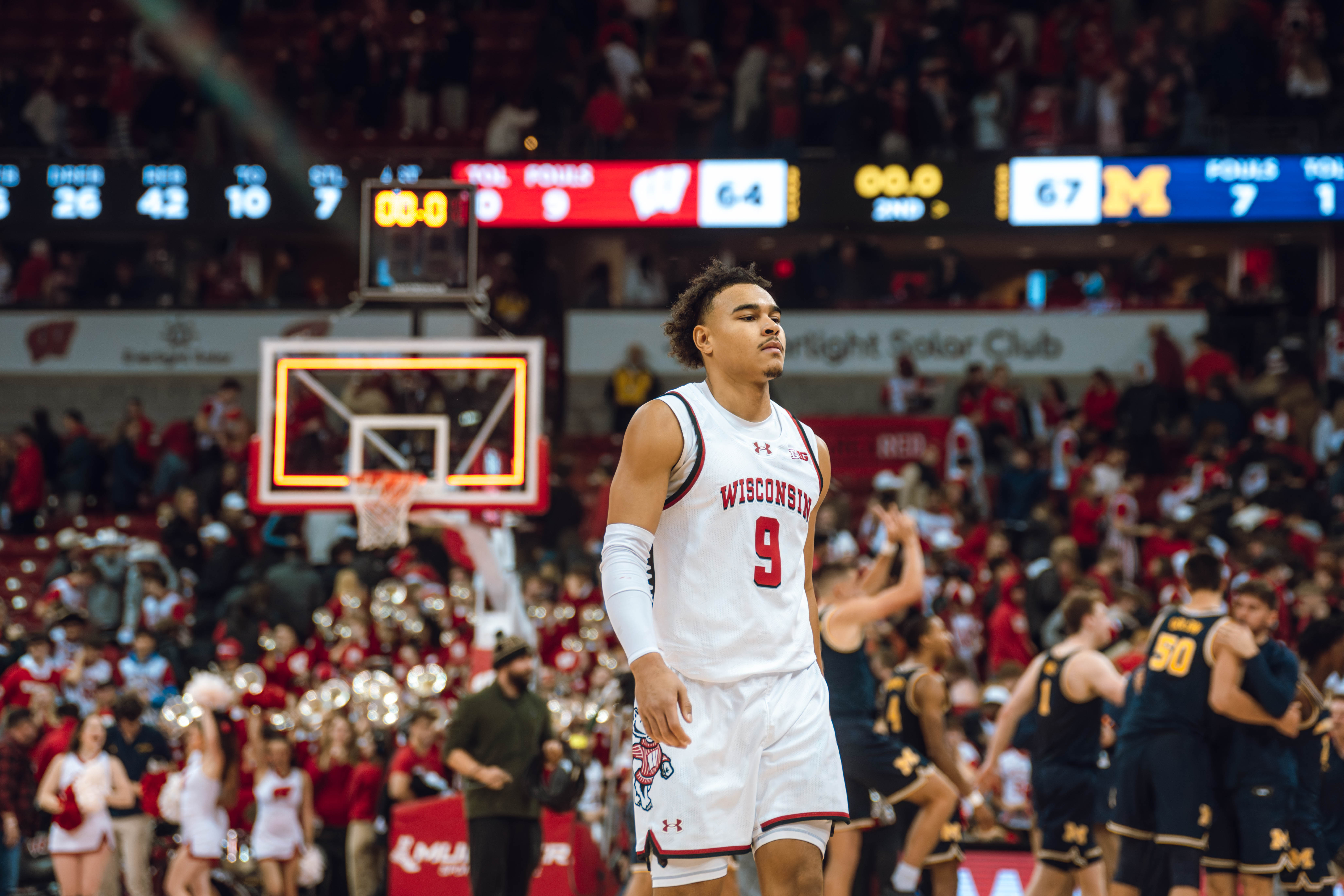 Wisconsin Badgers guard John Tonje #9 heads off the court as the Michigan Wolverines celebrate their win in the background at the Kohl Center on December 03, 2024 in Madison, Wisconsin. Photography by Ross Harried for Second Crop Sports.