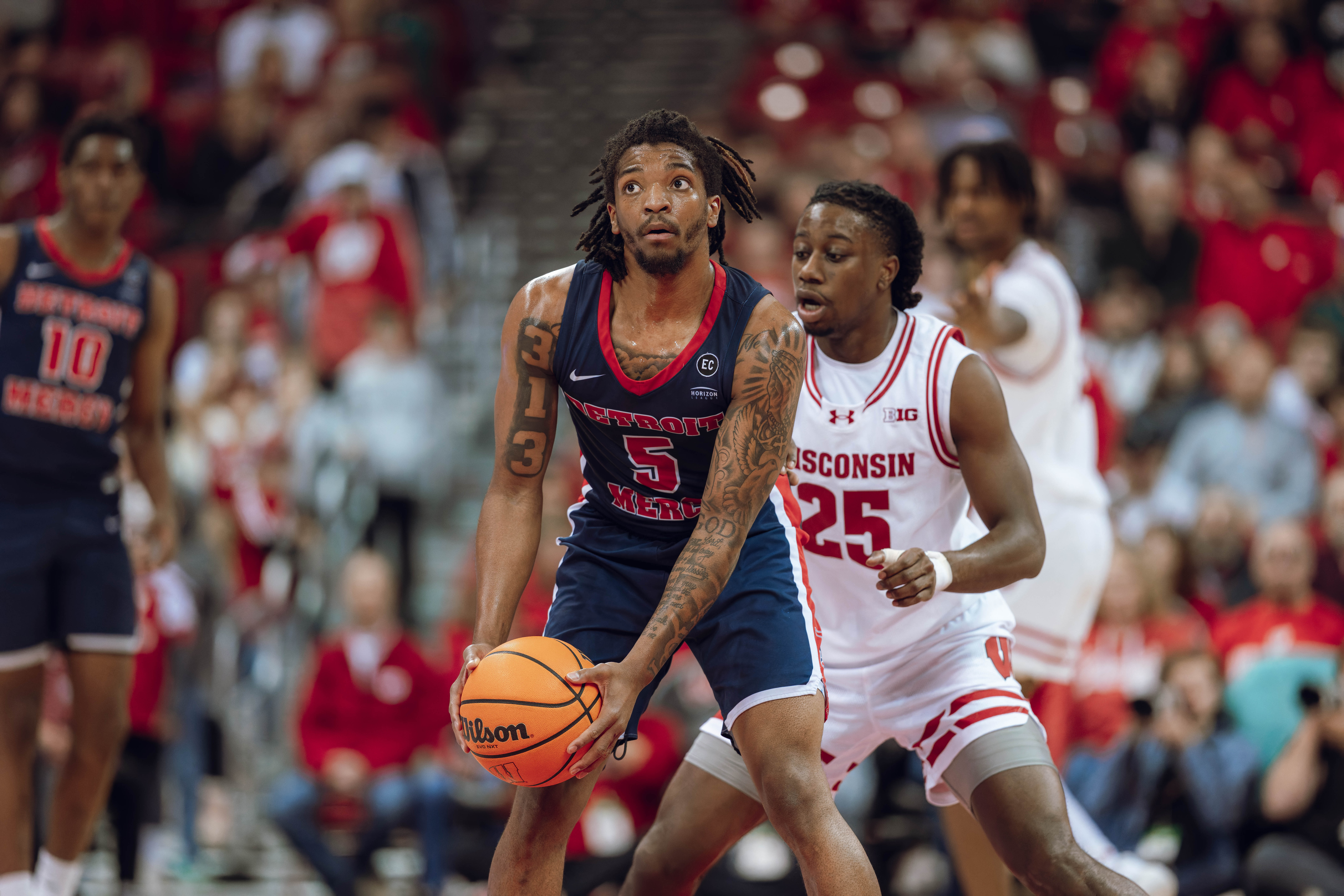 Detroit Mercy Titans guard Orlando Lovejoy #5 looks up at the game clock while being defended by Wisconsin Badgers guard John Blackwell #25 at Kohl Center on December 22, 2024 in Madison, Wisconsin. Photography by Ross Harried for Second Crop Sports.