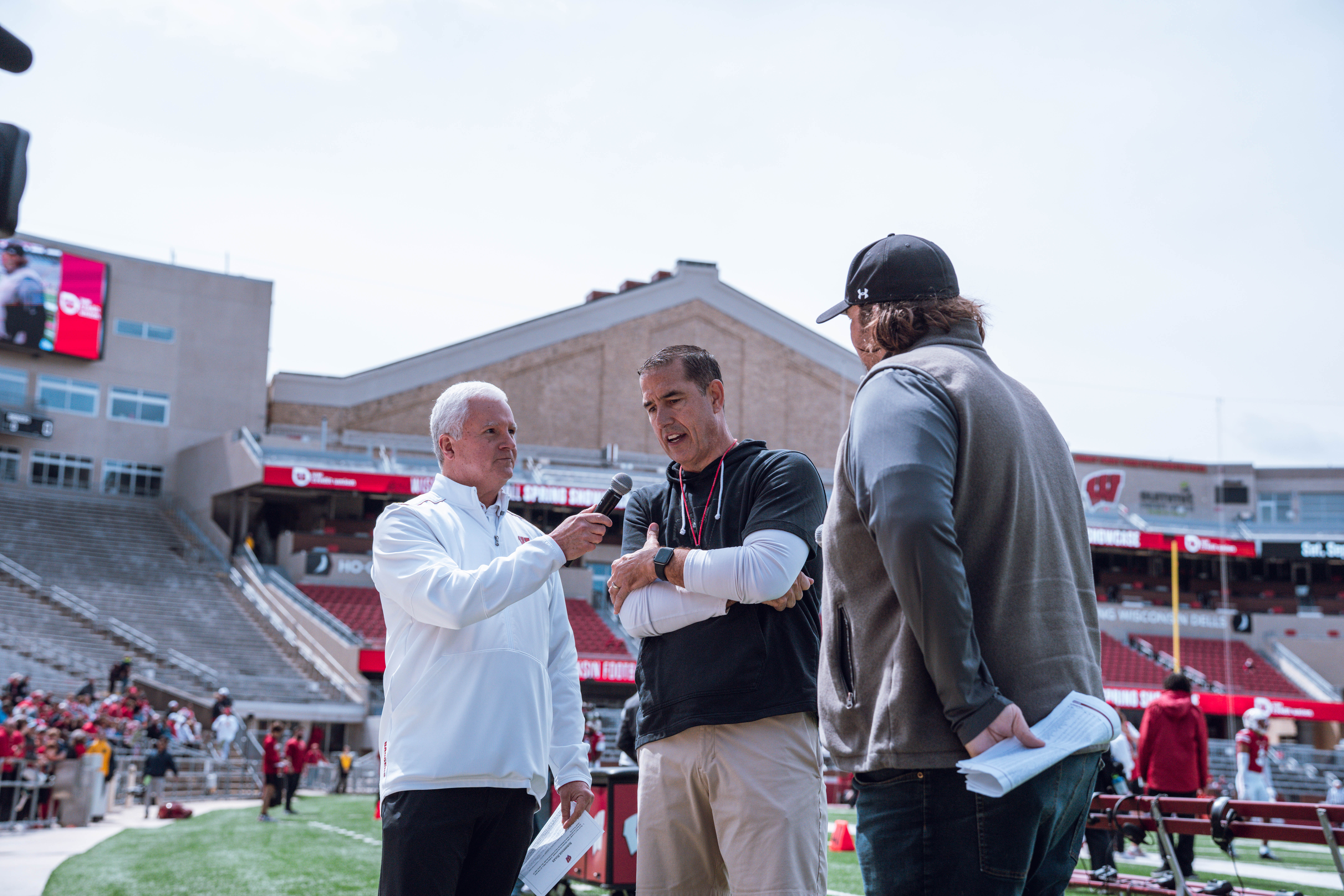Wisconsin Badgers head coach Luke Fickell (center) is interviewed by Matt Lepay (left) and Mark Tauscher (right) ahead of the Wisconsin Football Spring Showcase at Camp Randall Stadium on April 19, 2025 in Madison, Wisconsin. Photography by Ross Harried for Second Crop Sports.