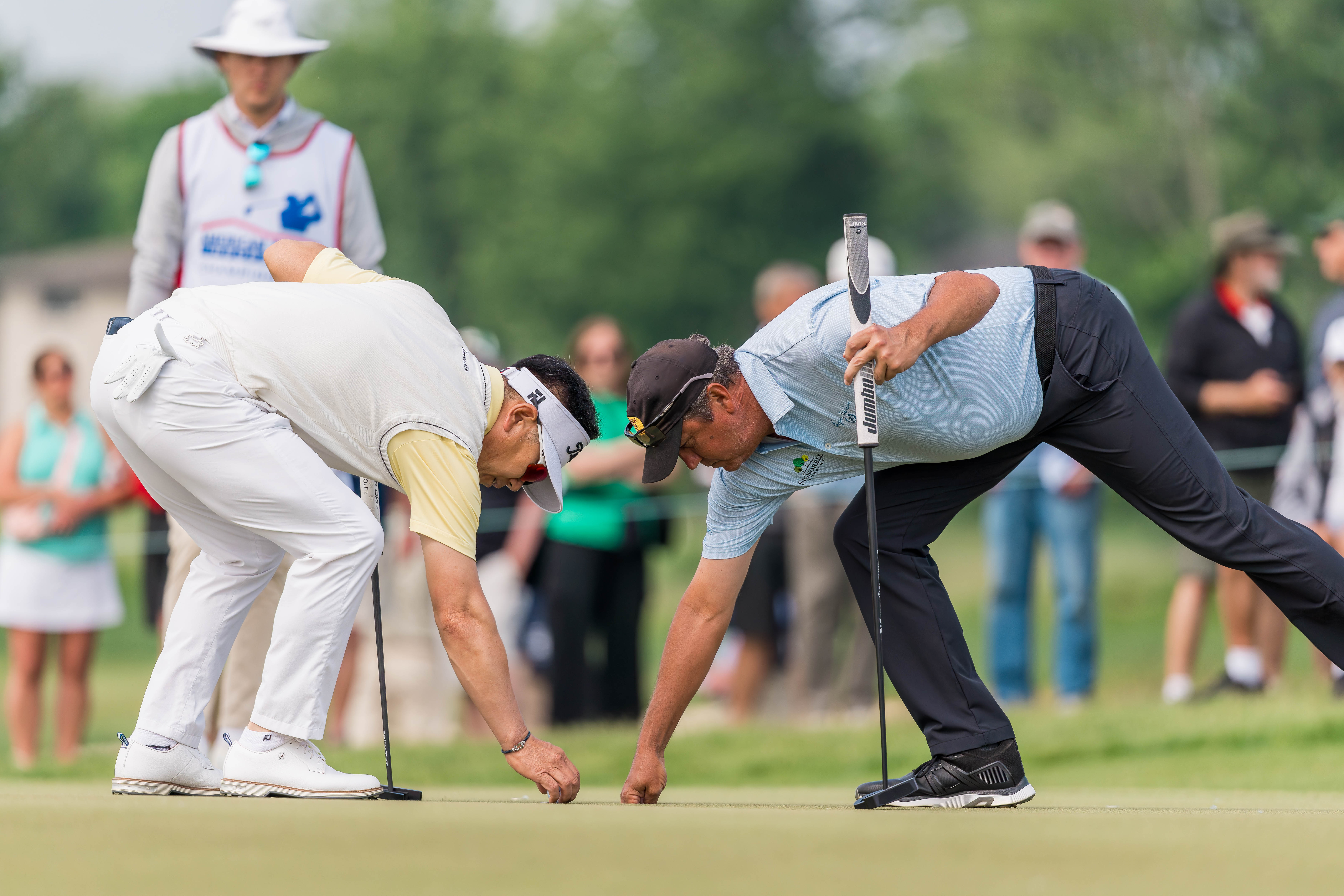 Shane Bertsch (right) retrieves his ball fro the cup while Y.E. Yang (left) places his ball for a putt on hole 1 during round 1 of The American Family Insurance Championship at TPC Wisconsin in Madison, Wisconsin on June 6th, 2025. Photography by Ross Harried for Second Crop Sports.