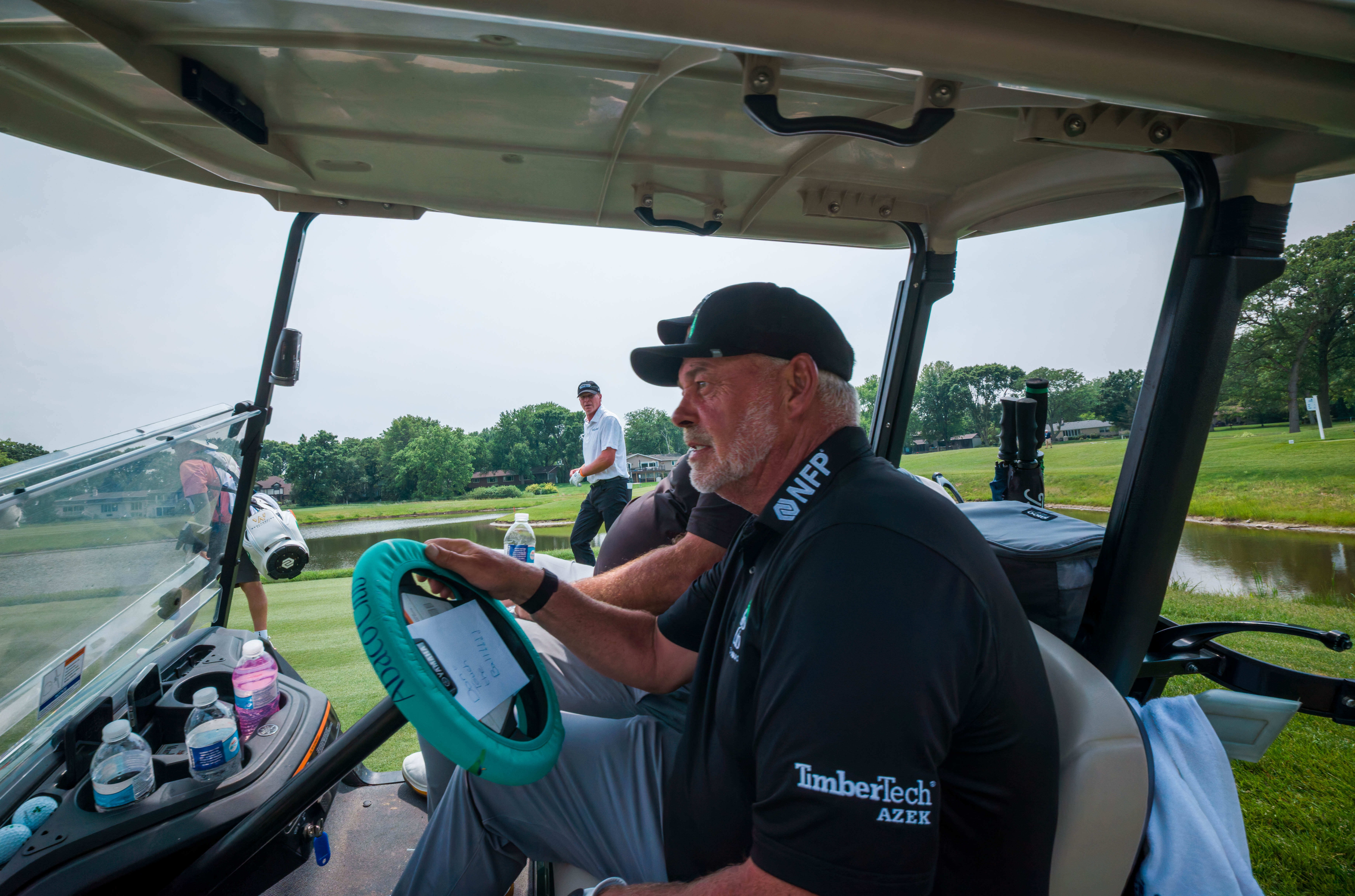 Darren Clarke drives a golf cart (foreground) as Steve Stricker looks on (background) during round 3 of The American Family Insurance Championship at TPC Wisconsin in Madison, Wisconsin on June 8th, 2025. Photography by Ross Harried for Second Crop Sports.