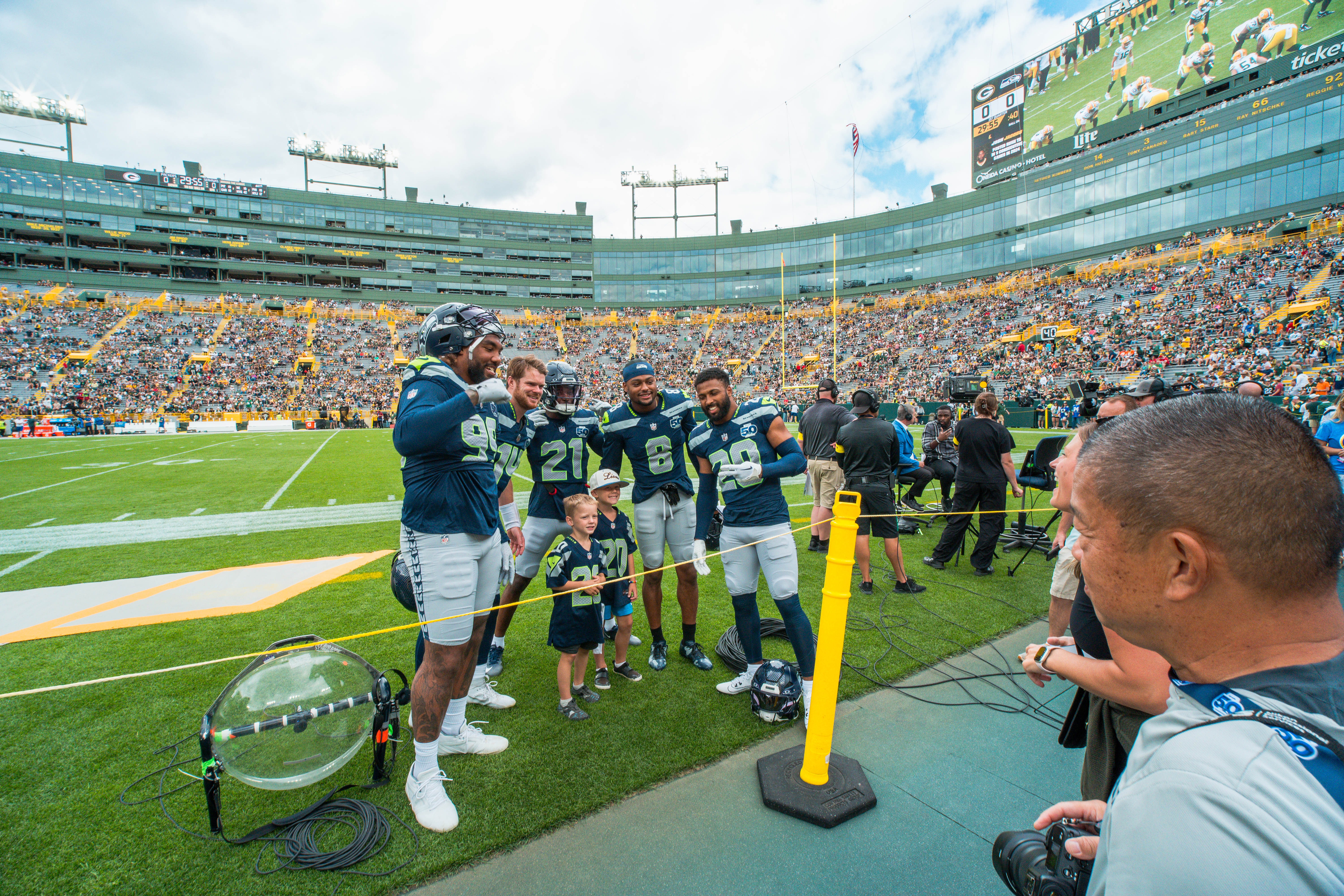 Seattle Seahawks defensive end Leonard Williams (99), quarterback Sam Darnold (14), cornerback Devon Witherspoon (21), Jalen Milroe (6) and safety Julian Love (20) pose for a fan photo before taking on the Green Bay Packers at Lambeau Field on August 23, 2025 in Green Bay, Wisconsin. Photography by Ross Harried for Second Crop Sports.